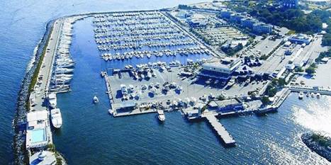 Hava görüntüsüyle bir marinanın genel görünümü, birçok yat ve tekneyle dolu, deniz kenarında yer alan park alanları.