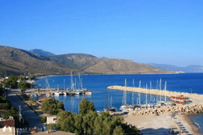 Bir liman manzarası, mavi deniz ve dağlarla çevrili. Birkaç yelkenli tekne ve kayık limanda demirlemiş.